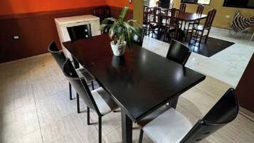 Un comedor con una mesa larga y varias sillas, una planta en maceta sobre la mesa y un cuadro en la pared.