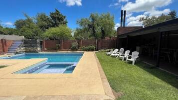A backyard with a swimming pool, a covered patio area, and a brick wall.