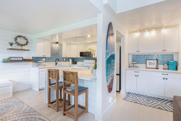 A modern kitchen with white cabinetry, a blue backsplash, and a surfboard decoration.