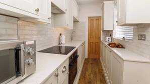 A compact kitchen with white cabinetry, a built-in oven, a stovetop, and a wooden door. - Walpole Retreat - Hot Tub, Games Room, Sleeps 4 (York)