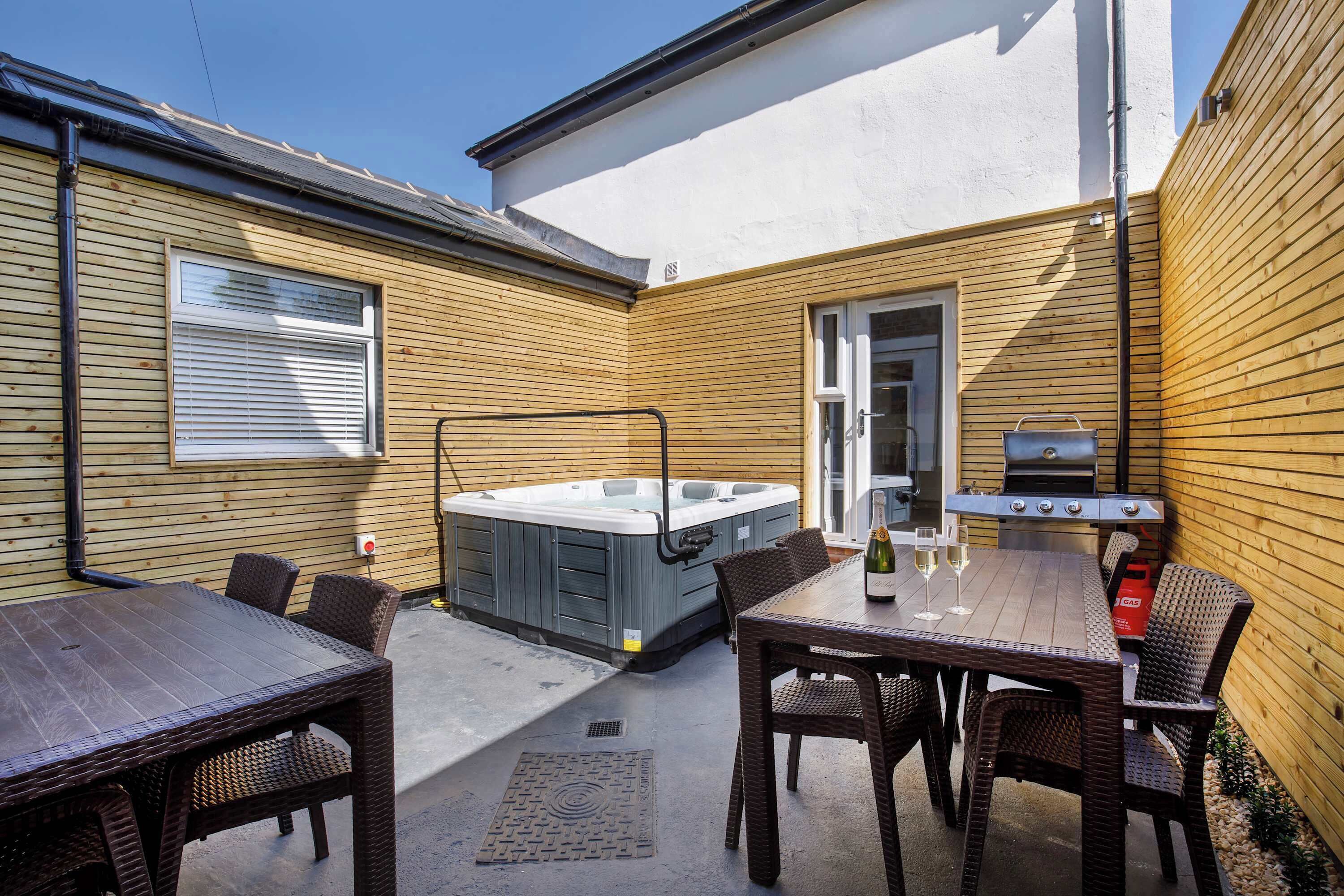 An outdoor patio with a hot tub, grill, and dining area.