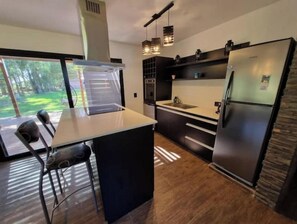 Una cocina moderna con una isla grande, armarios negros, electrodomésticos de acero inoxidable e iluminación colgante.