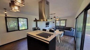 Una cocina moderna con una isla central, estufa integrada e iluminación colgante. Hay dos ventanas amplias que ofrecen luz natural y vistas al exterior.
