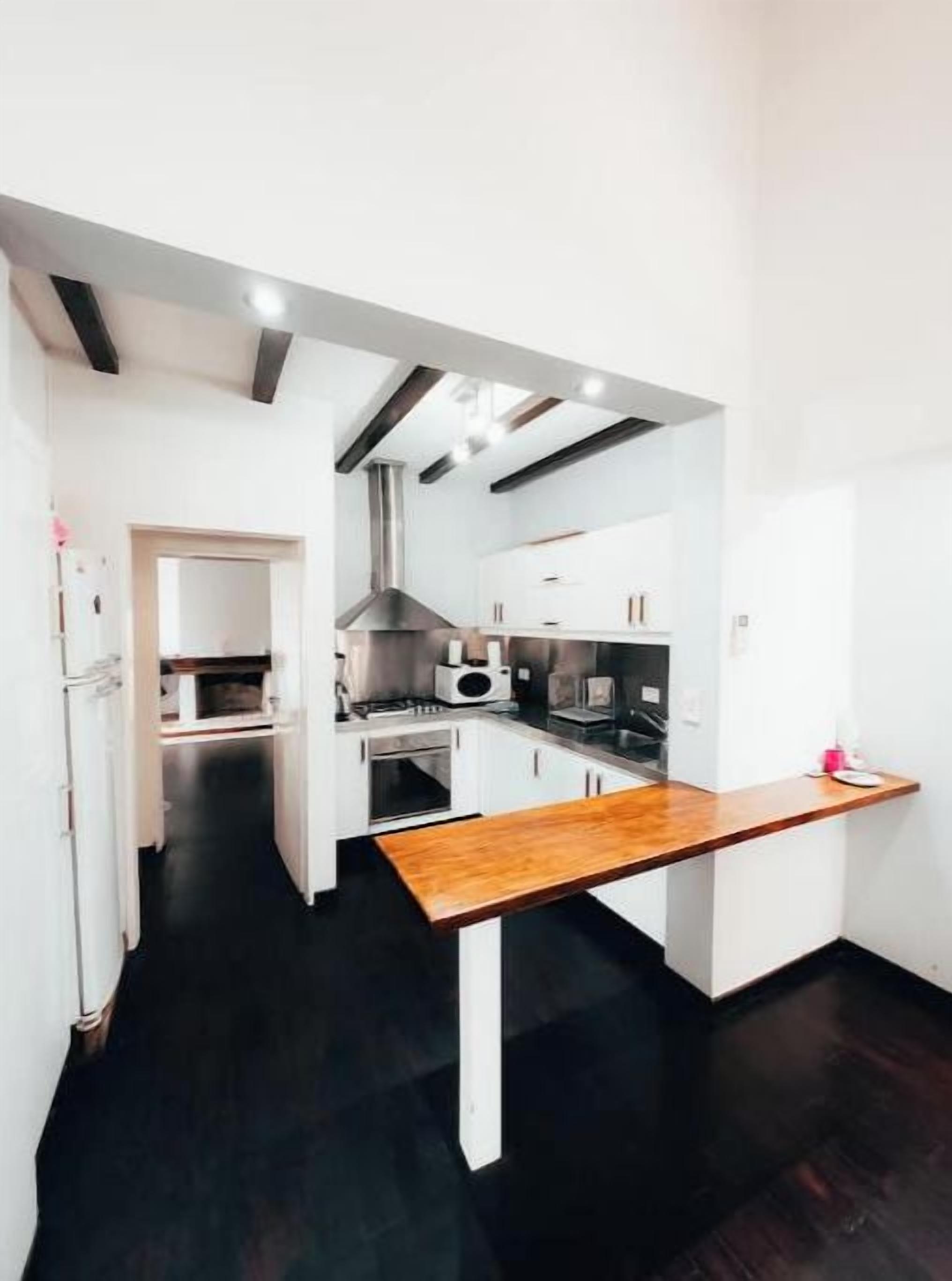 Une cuisine moderne avec des meubles blancs, un plan de travail en bois et un sol noir.