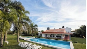 Une maison moderne avec une piscine, entourée de palmiers et d’une pelouse bien entretenue.