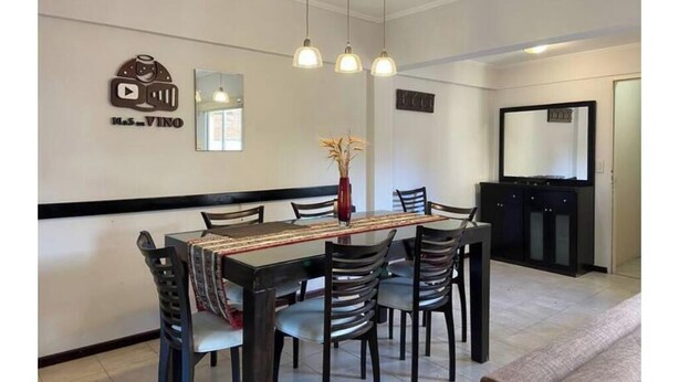 A dining area with a table, chairs, pendant lights, a vase with dried flowers, a mirror, and a cabinet. - Central quality full terrace own grill (Paraná)