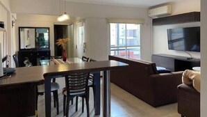 A modern living room with a dining area, a sofa, a TV, and a large window providing natural light. - Central quality full terrace own grill (Paraná)