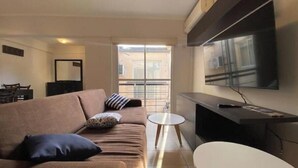 A modern living room with a brown sofa, a small round table, and a large TV mounted on the wall. - Central quality full terrace own grill (Paraná)