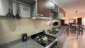A kitchen with granite countertops, a gas stove, and stainless steel appliances. There are hanging utensils and a microwave above the stove. - Central quality full terrace own grill (Paraná)