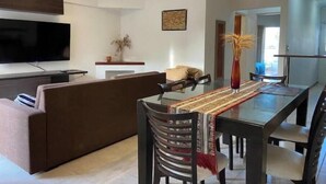 A modern living room with a sofa, a dining table with chairs, a TV mounted on the wall, and pendant lights. - Central quality full terrace own grill (Paraná)