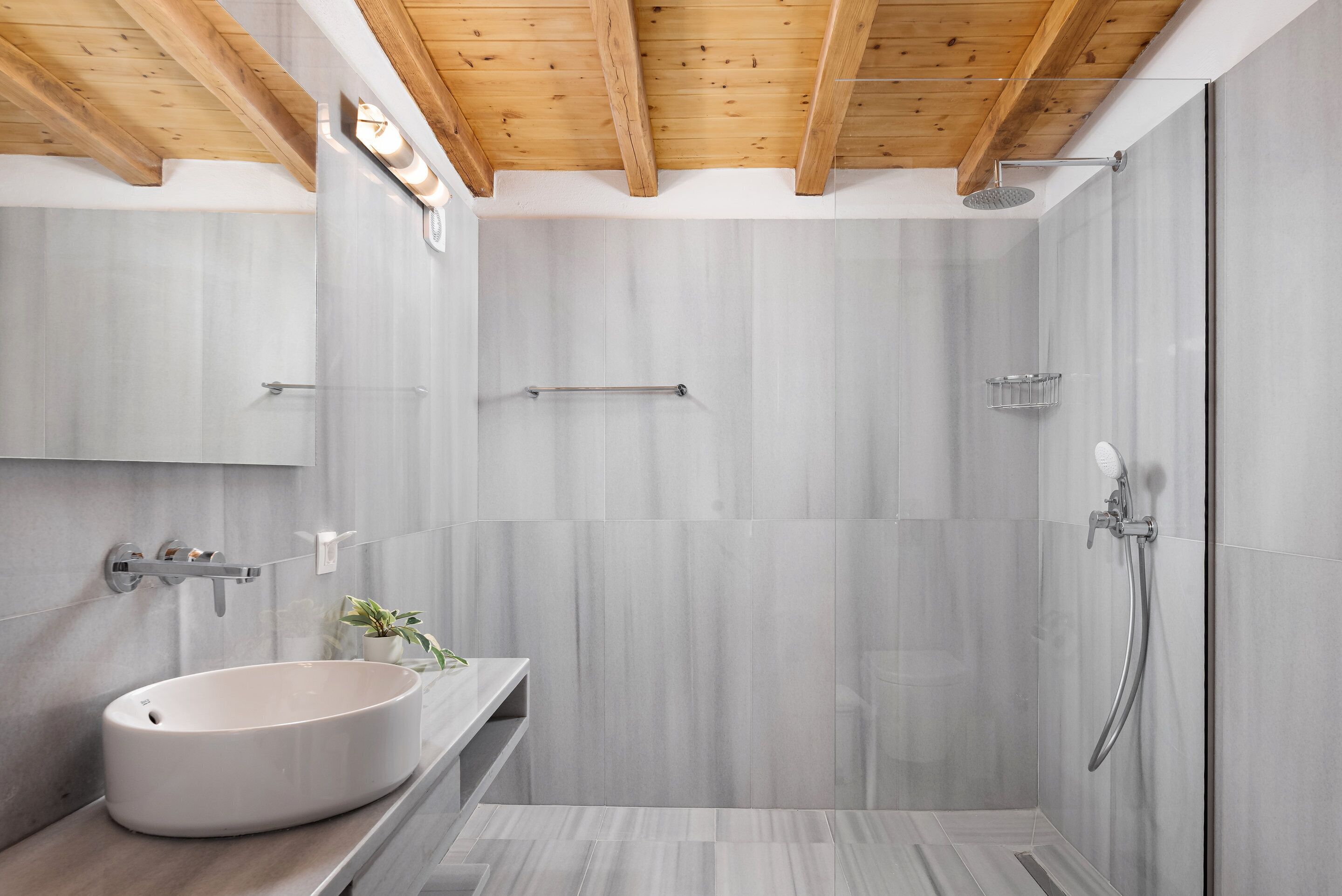 A modern bathroom with a large white sink, a glass shower enclosure, and wooden ceiling beams.