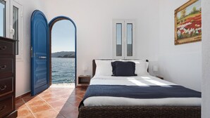 A bedroom with a bed, a dresser, a blue door, a window, and a painting. - Porto Castello Villas (Skiathos)