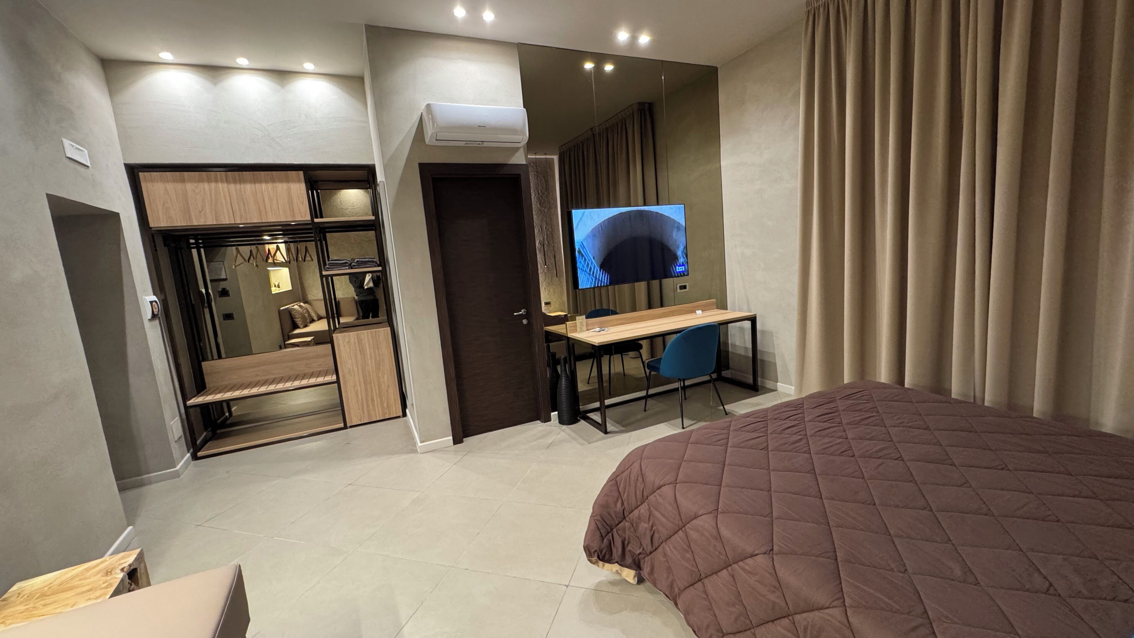 A modern hotel room with a large bed, a desk, a television, and a wardrobe.