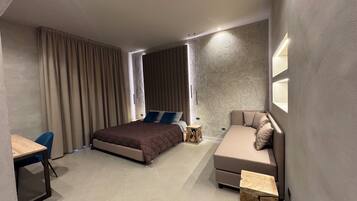 A modern hotel room with a large bed, a sofa, a desk, and a small side table.