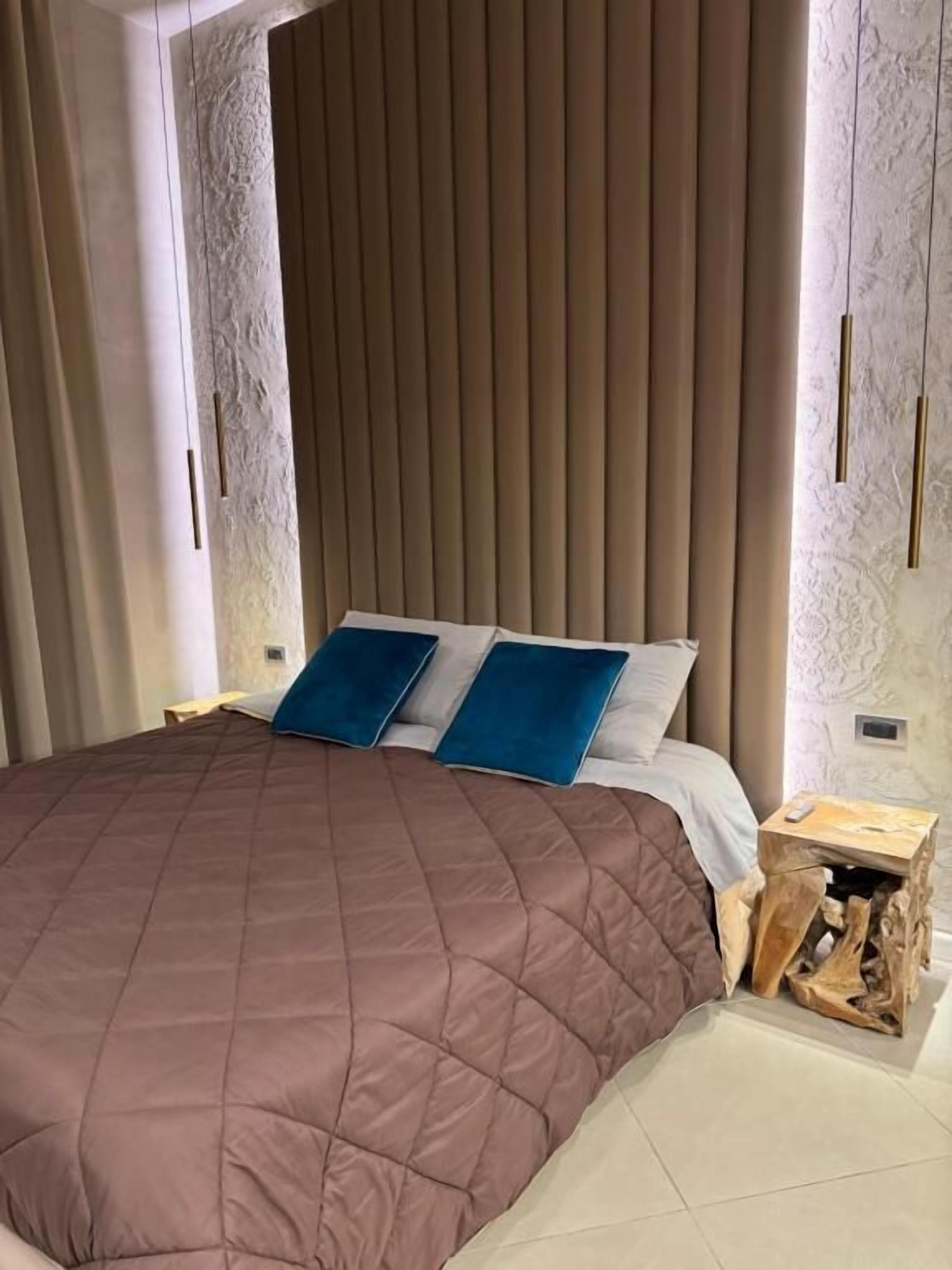 A modern bedroom with a large bed, a wooden headboard, and a nightstand with a lamp.