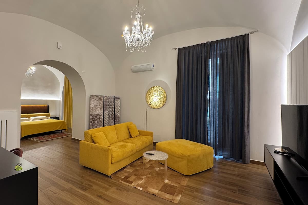 Un salon moderne avec un canapé jaune, une table basse ronde et un lustre.