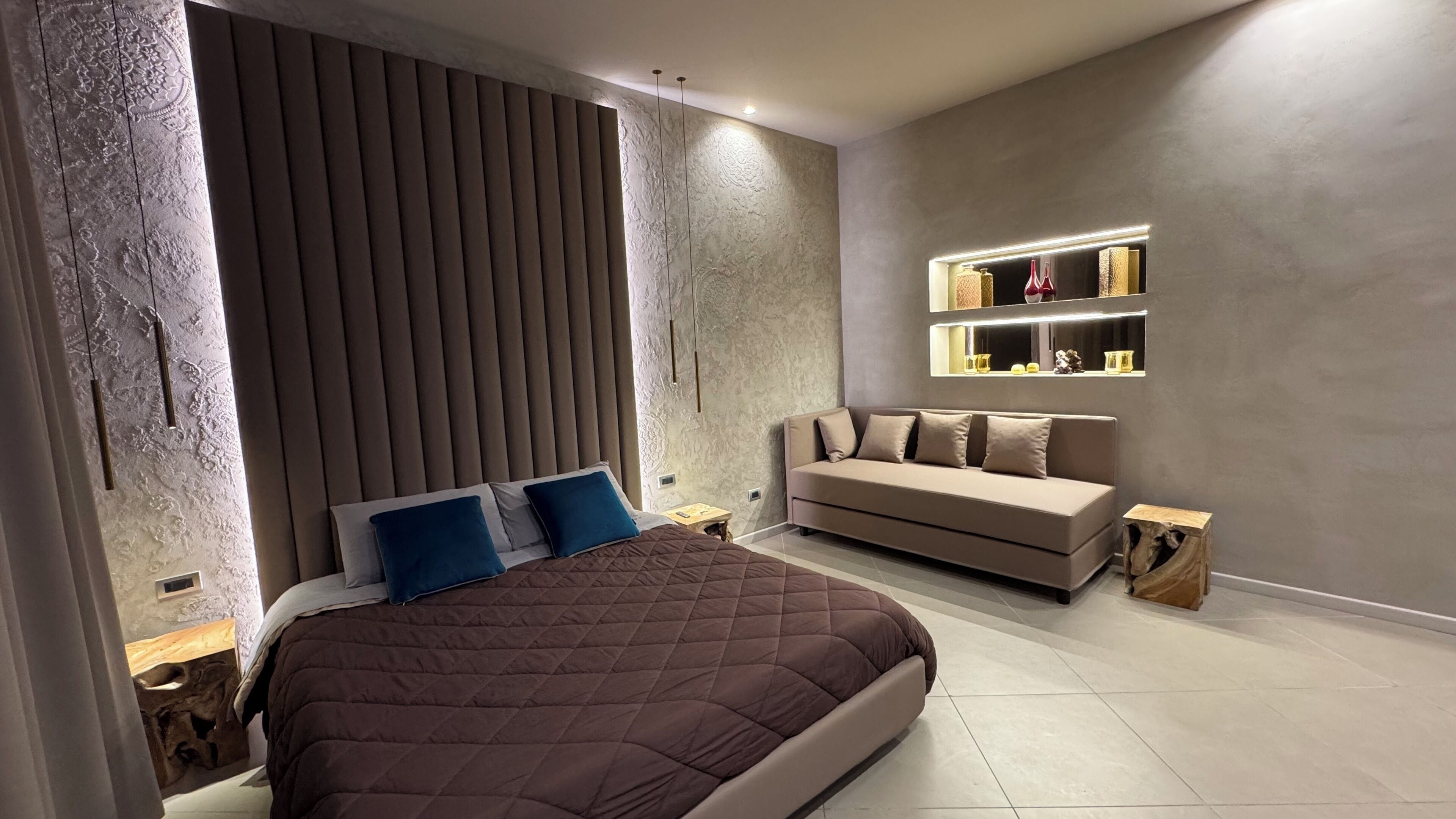 A modern bedroom with a large bed, a sofa, and built-in shelves.