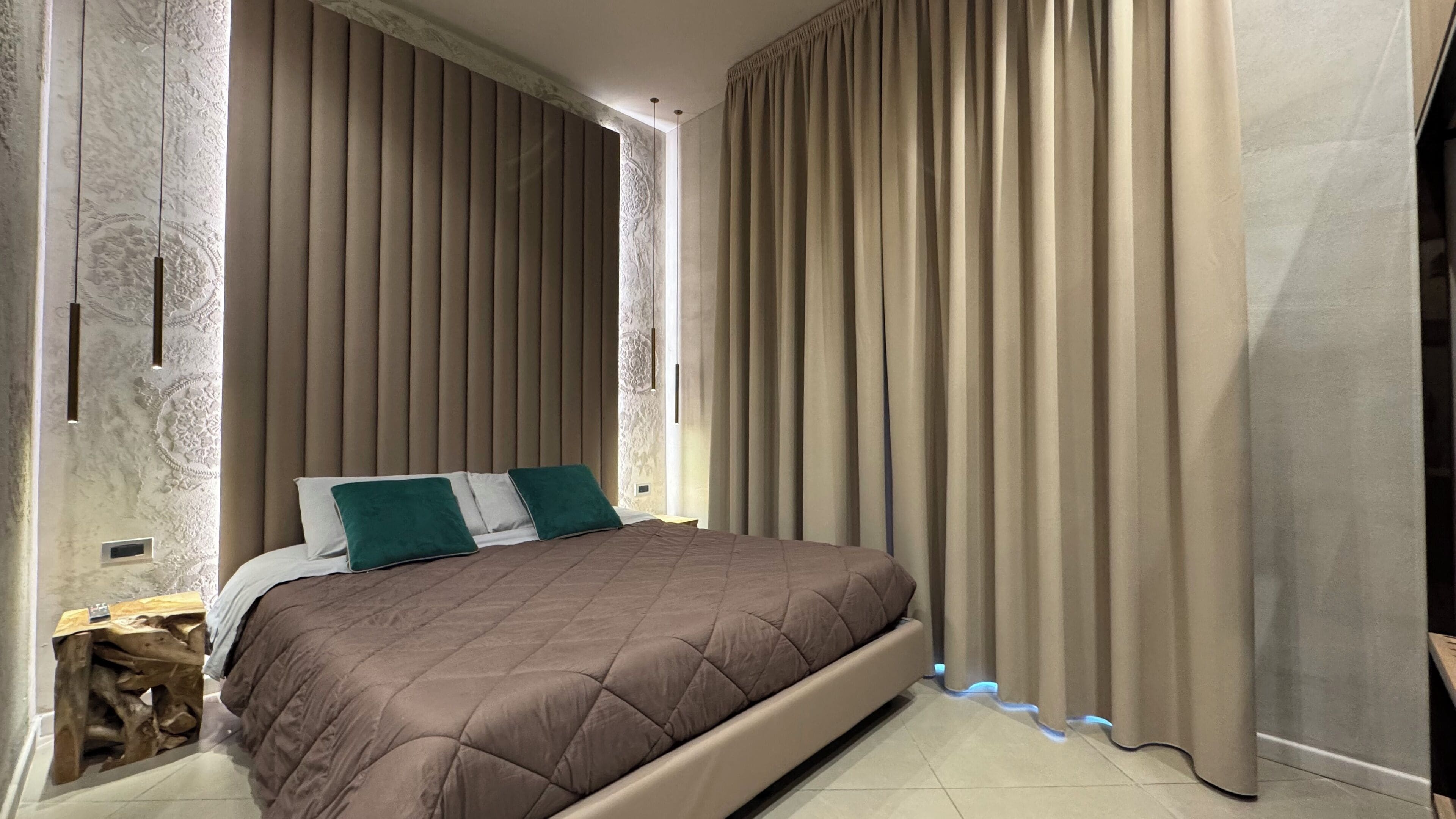Un dormitorio con una cama grande, cortinas color beige y una pared con textura.