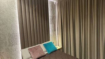 A bedroom with a large bed, a nightstand, and a window with curtains.