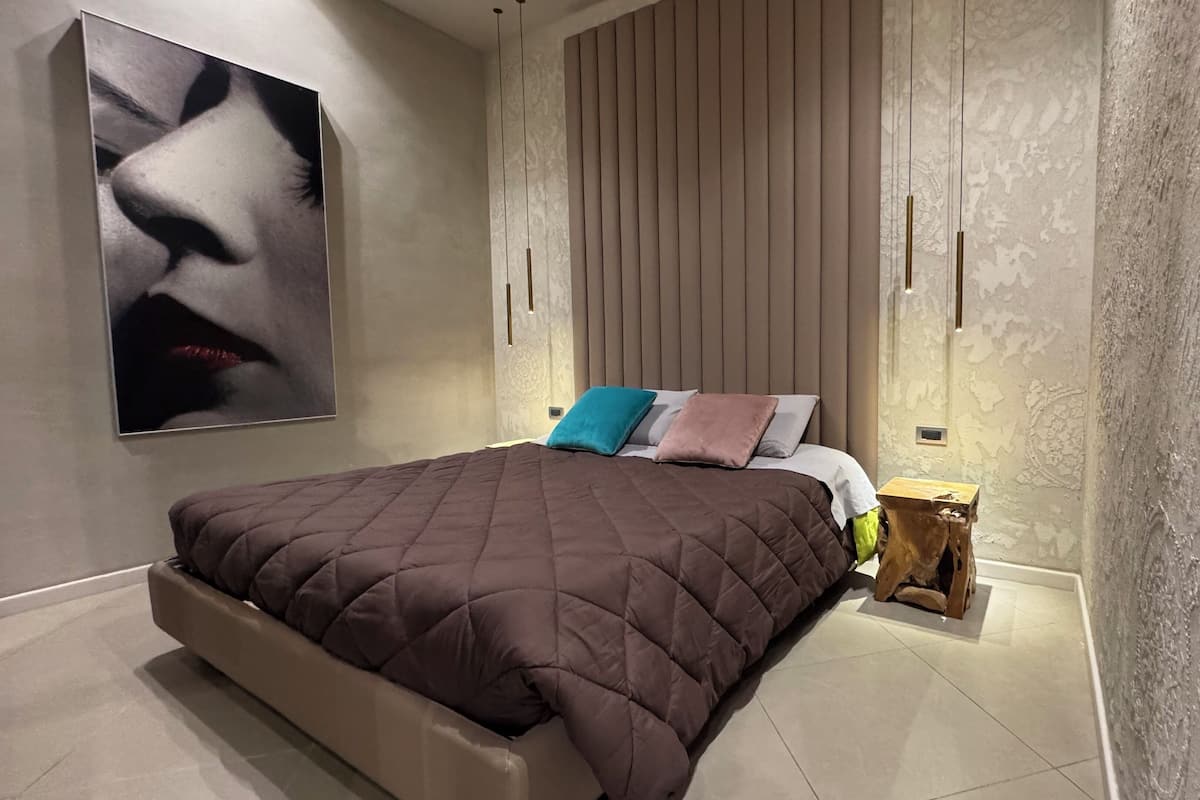 Une chambre à coucher moderne avec un grand lit, une tête de lit à lattes verticales et un luminaire fixé au mur.
