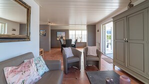 Un salon comprenant un canapé, deux fauteuils, une table basse et un meuble. Un téléviseur est fixé au mur et il y a une fenêtre avec vue.
