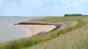 Un paysage côtier avec une plage de sable, des dunes herbeuses et un bâtiment en arrière-plan.
