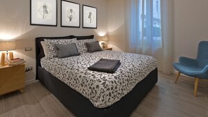 Un dormitorio moderno con una cama grande, mesitas de noche, un sillón azul y tres cuadros enmarcados en la pared.