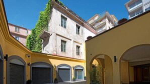 Un patio con tres puertas de garaje cerradas, un edificio amarillo y un edificio blanco con una enredadera verde.
