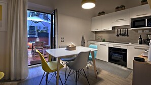 A modern kitchen with white cabinets, a microwave, and a coffee machine. There is a dining area with a white table and chairs. - Le terrazze sul cortile - Red (Salerno)