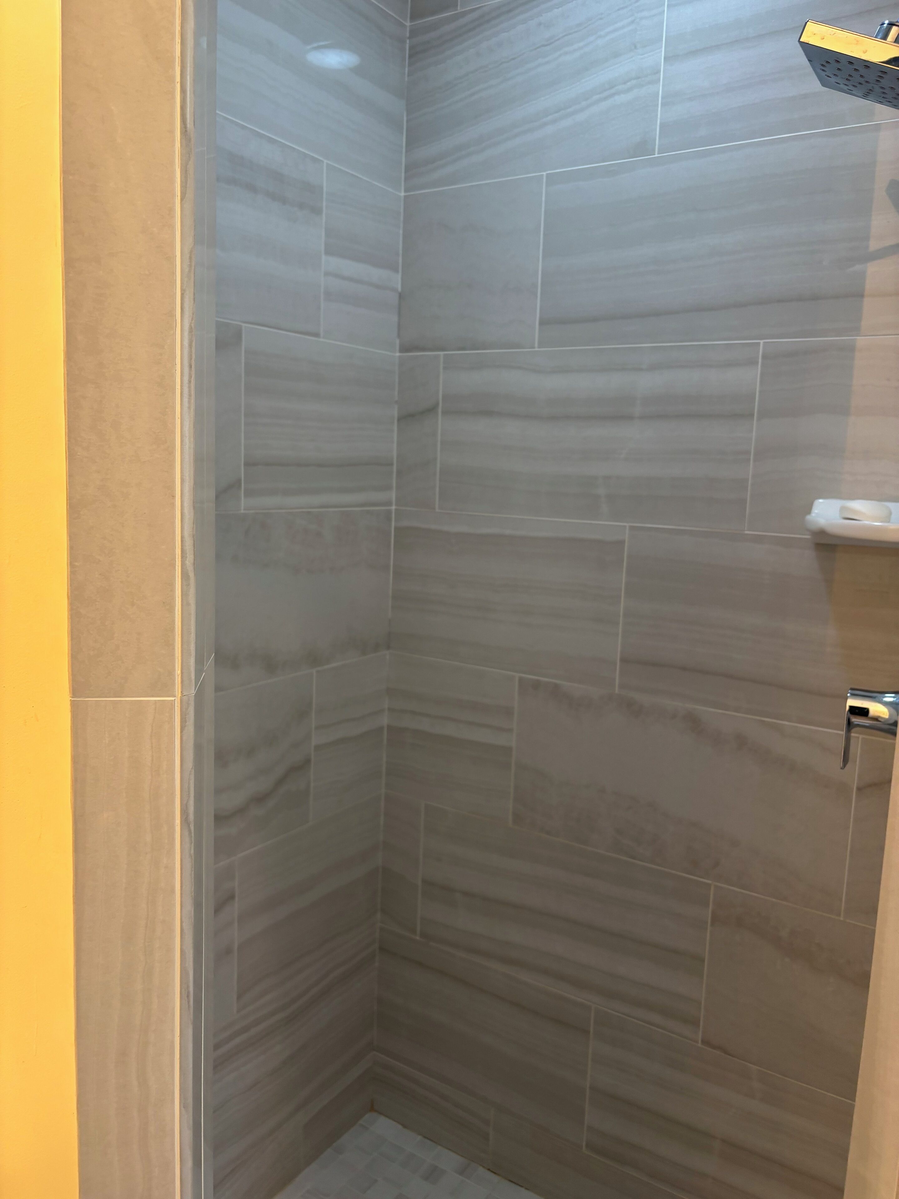 A corner shower with grey tiles and a white soap dish on the wall.