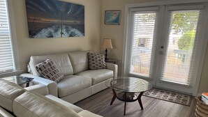 Un salon avec un canapé en cuir beige, une table basse en verre et un tableau représentant une mer déchaînée.