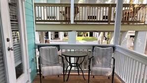 Une terrasse en bois avec un porche couvert, deux chaises à rayures et une petite table.