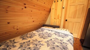 A bedroom with wooden walls, a bed with a floral bedspread, and a wooden door. - aframe in the woods. (Emsdale)