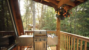 A wooden deck with a barbecue grill and hanging flower baskets. - aframe in the woods. (Emsdale)