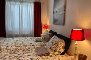 Une chambre à coucher avec une couvre-lit à motifs floraux, deux oreillers, une lampe rouge et un tableau accroché au mur.