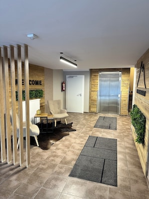 A modern lobby with a reception desk, a fire extinguisher, a white door, an elevator, and a reception wall with a 'WELCOME' sign. - Alpinresort Kaprun Top 2: Skiing from October to the end of May. (Kaprun)