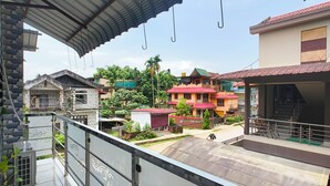 A balcony with a metal railing, a covered area with a corrugated metal roof, and a view of surrounding buildings and greenery.