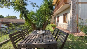 Une terrasse extérieure avec une table et des chaises en bois, entourée de verdure et donnant sur un bâtiment doté d’un balcon.