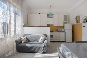 A compact living space with a sofa, a dining table, a kitchenette, and a window with patterned curtains.