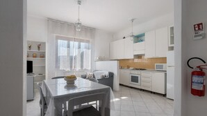 Une cuisine moderne avec des meubles blancs, un four à micro-ondes et un évier. On y trouve une table à manger avec des chaises et une fenêtre avec des rideaux.