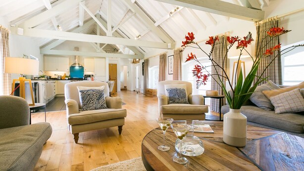 A spacious living room with high ceilings and exposed beams, a cozy seating area with sofas and armchairs, and a wooden coffee table with decorative items.