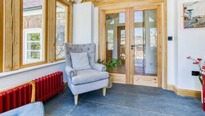 A cozy room with a grey upholstered armchair, a red radiator, and a large window.