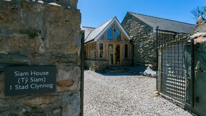 A stone building labeled 'Siam House (Ty Siam) I Stad Clynog' with a gravel driveway and a metal gate.