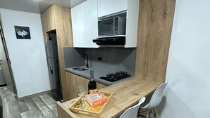A compact kitchen with a wooden island, white chairs, a microwave, and a wine bottle on the counter. - Loft studio apartment (Envigado)