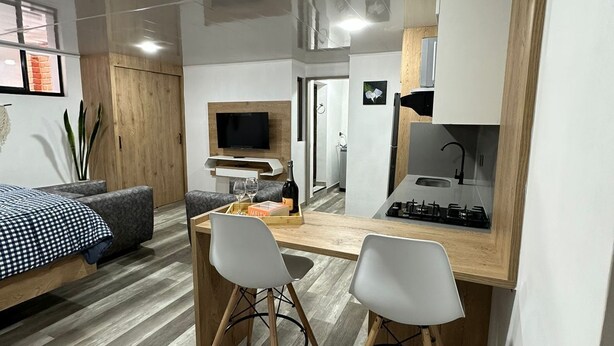 A modern, compact living space with a bed, a TV, a dining area with two chairs, and a kitchen area with a stove. - Loft studio apartment (Envigado)