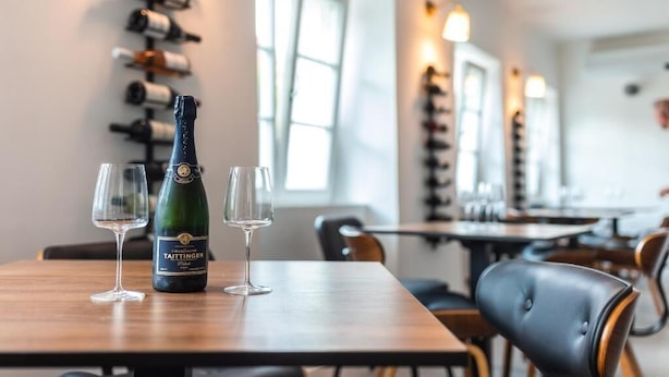 A restaurant interior with a wine rack, a bottle of Taittinger champagne, and two glasses on a table. - Hiša OPERA (Maribor)