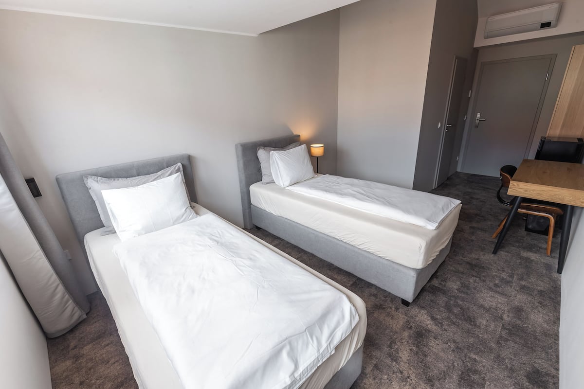 A hotel room with two single beds, a desk, and a chair.