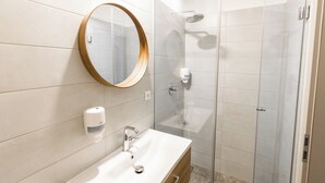 A modern bathroom with a white sink, a round mirror, and a glass-enclosed shower. - Hiša OPERA (Maribor)