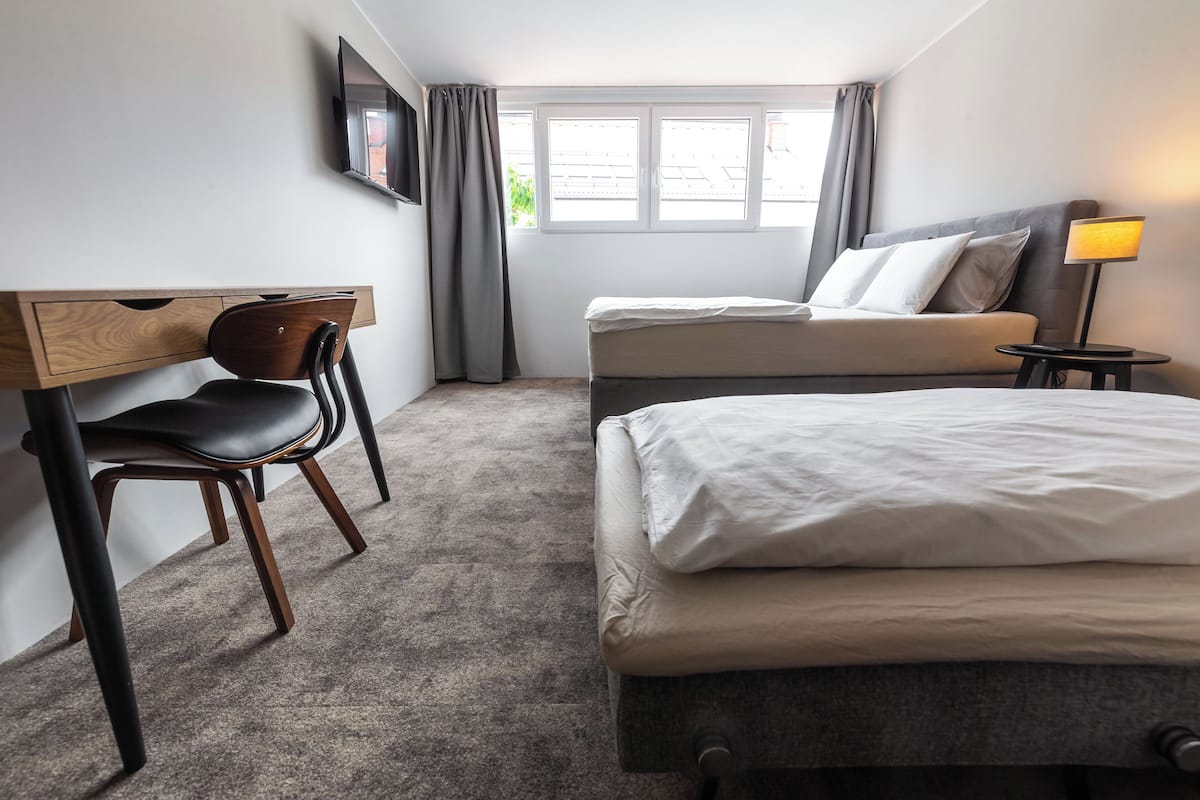 A hotel room with a desk, two beds, a TV, and a lamp.