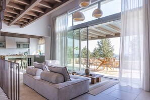 A modern living room with a grey sofa, a dining area with wooden chairs, and a kitchen in the background. - Bacchetta Magica - Four Bedroom Villa, Sleeps 8 (Paxi)